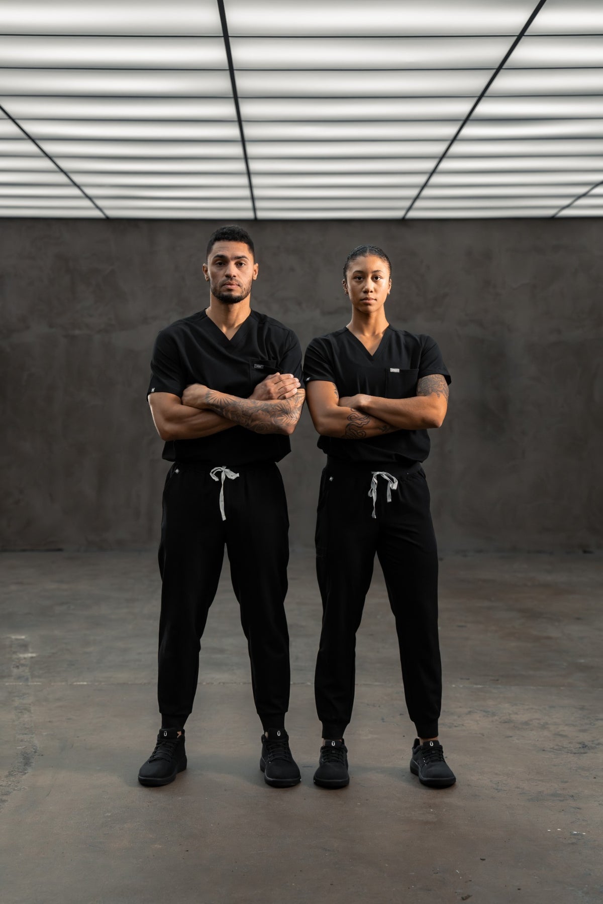 Two nurses in black scrubs and Perform Blackout, arms crossed on a cement floor