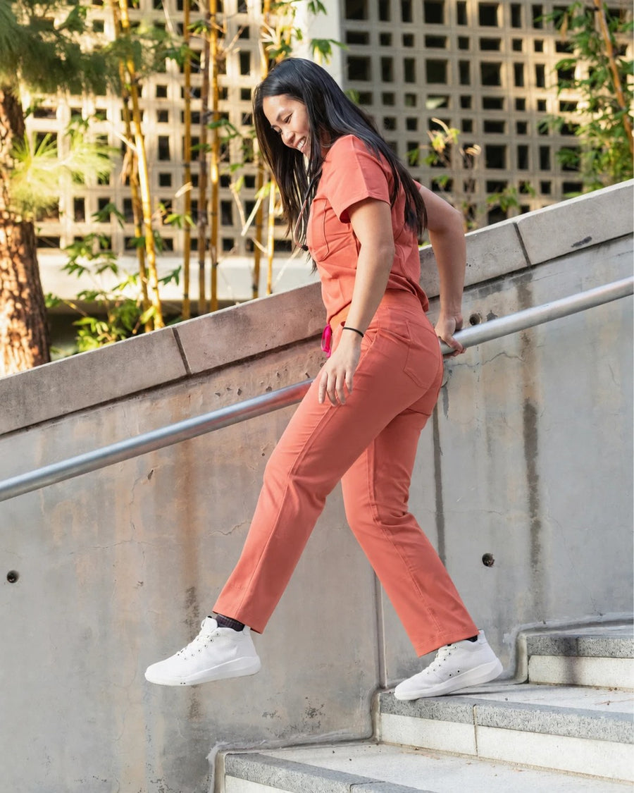 Healthcare worker in coral scrubs on outdoor stairs in Perform Whiteout Mid