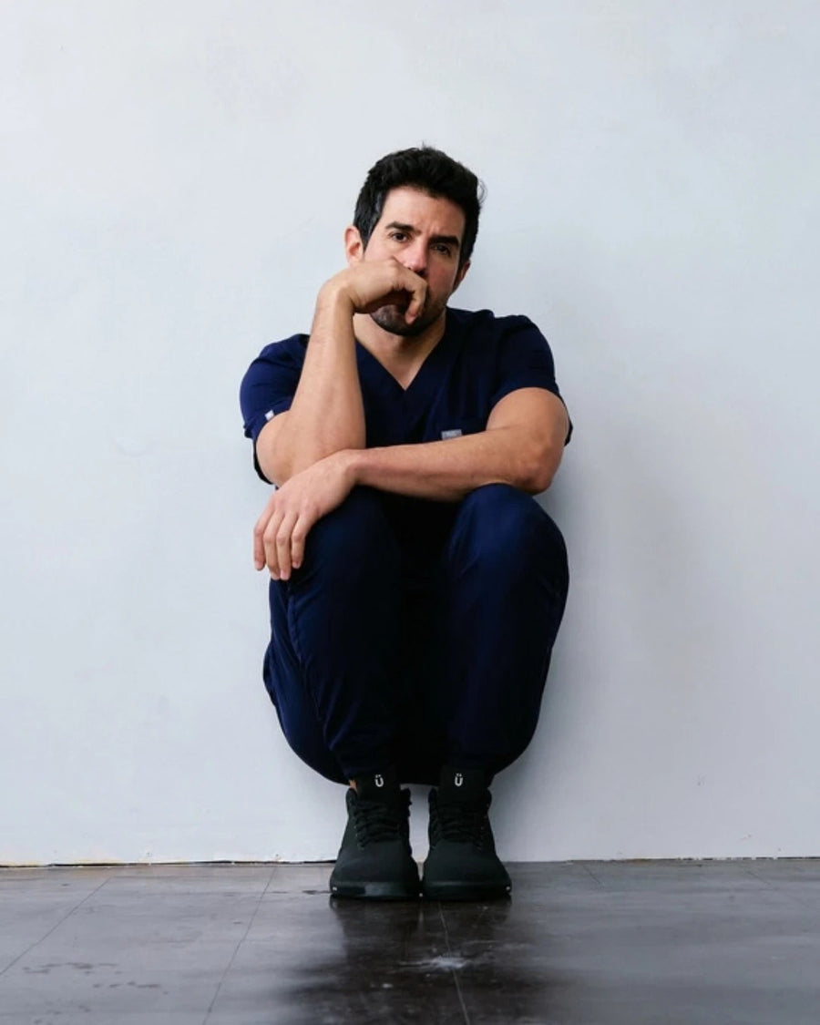 Healthcare worker in navy scrubs sitting against a wall in Perform Blackout