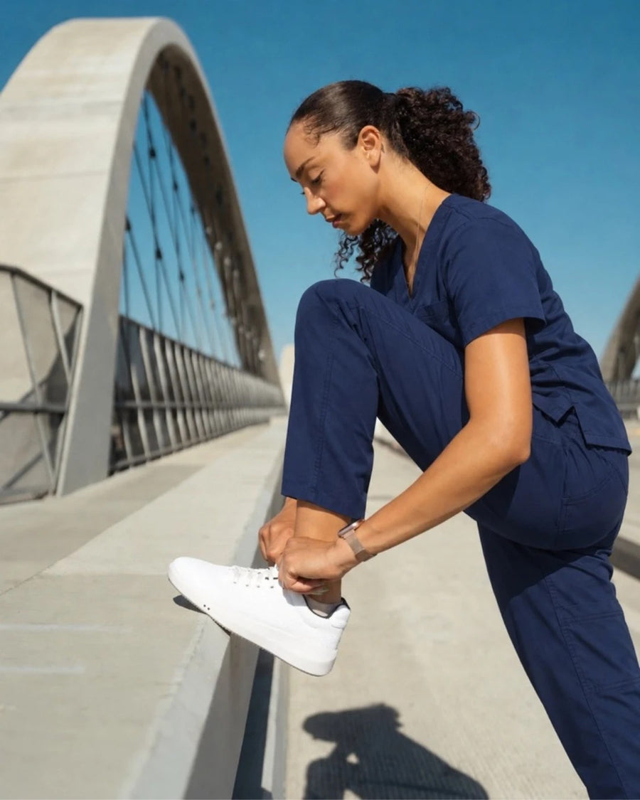 Healthcare worker in navy scrubs lacing Perform Whiteout Low on a bridge