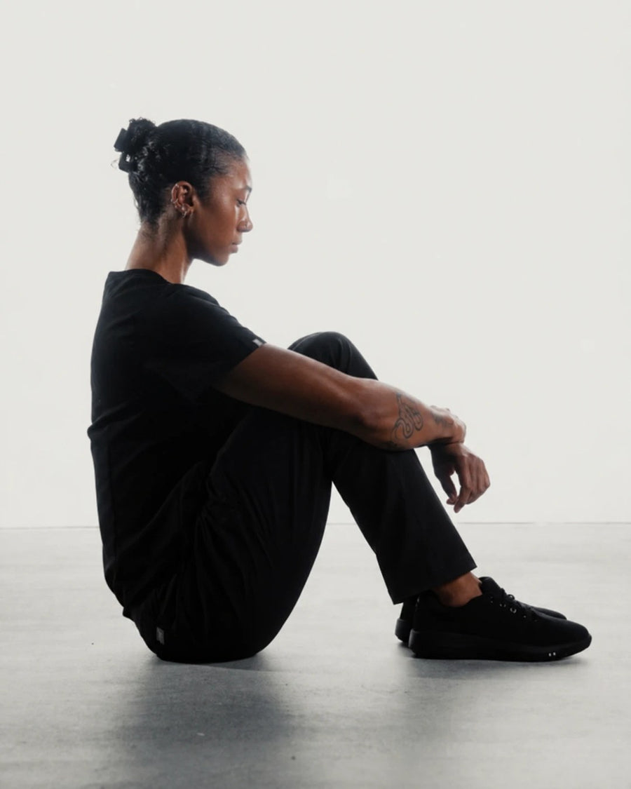 Healthcare worker in black scrubs sitting on the floor in Perform Blackout Low