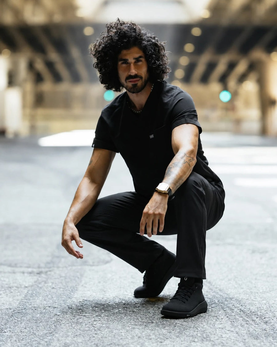 Healthcare worker in black scrubs crouching in the street in Perform Blackout Mid